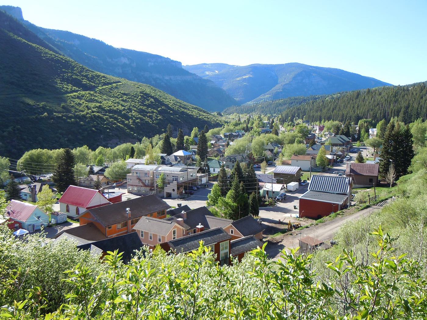 The town of Minturn, Colorado, seen from a hillside: a few streets of small coloured houses along a valley floor, with forested ridgelines rising on both sides.